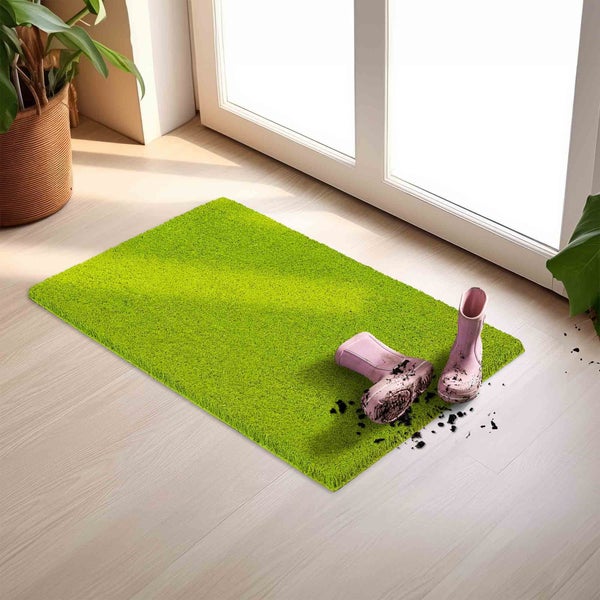 Grüne Fußmatte vor einer Tür mit zwei schmutzigen Gummistiefeln darauf