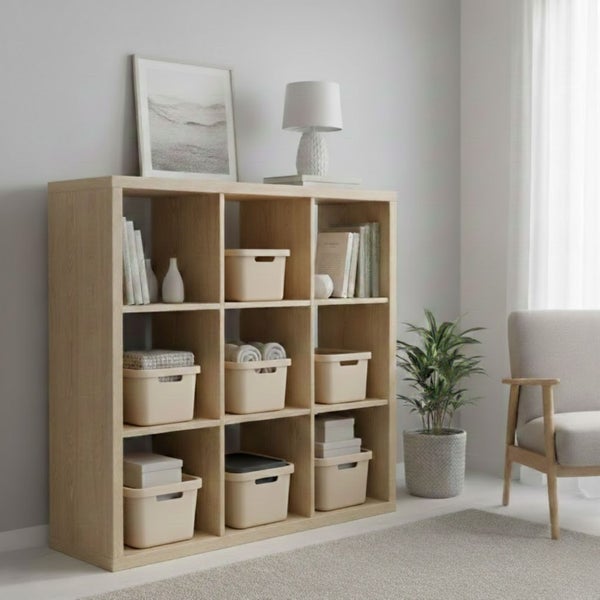 Regal mit neun Fächern, gefüllt mit Büchern und Aufbewahrungsboxen, neben einer Zimmerpflanze und einem Sessel