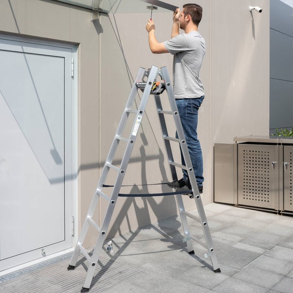 Eine Person steht auf einer Klappleiter und montiert ein Vordach an einem Gebäude.