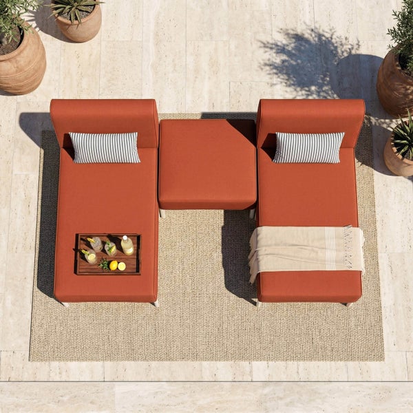 Modulares Garten-Lounge-Set in Terrakotta auf einem beigen Teppich mit gestreiften Kissen und Holztablett auf einer hellen Steinterrasse.