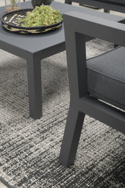 Moderne Outdoor-Lounge-Möbel bestehend aus einem quadratischen Beistelltisch und einem Sessel mit Polsterung auf einem gemusterten Außenteppich.