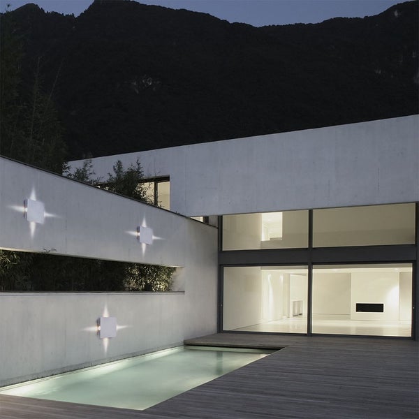 Moderne Hausfassade mit Außenbeleuchtung, Pool und Holzterrasse vor Bergkulisse