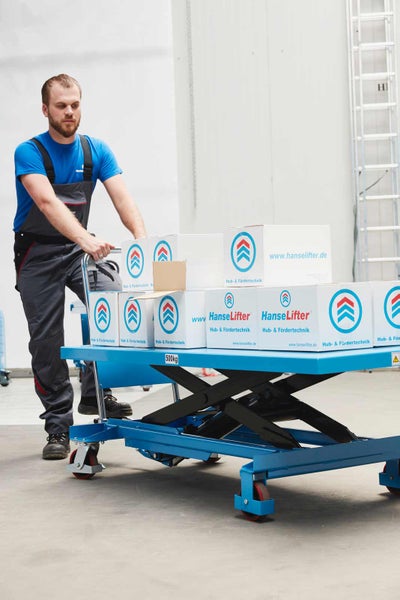 Ein Mann schiebt einen blauen Scherenhubtisch mit 500 Kilogramm Tragkraft, beladen mit weißen Kartons mit HanseLifter Logo.