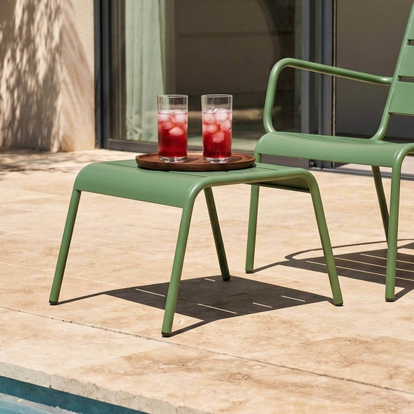 Grüner Gartenhocker oder Beistelltisch aus Metall auf einer Terrasse am Pool mit Getränken und passendem Gartenstuhl.