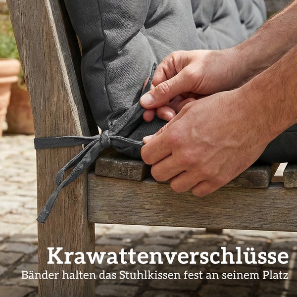 Eine Person befestigt ein Stuhlkissen mit Bindebändern an einem Holzstuhl.