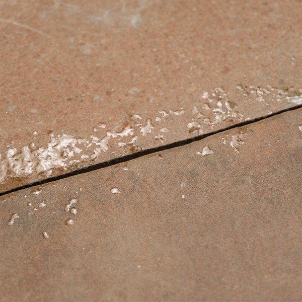Nahaufnahme von Bodenplatten mit einer Fuge und anhaftenden Rückständen von Fugenmörtel.