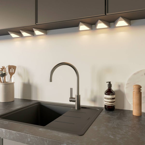Moderne Küche mit Edelstahl-Armatur, Spülbecken in Anthrazit und dreieckigen LED-Unterbauleuchten unter grauen Hängeschränken.