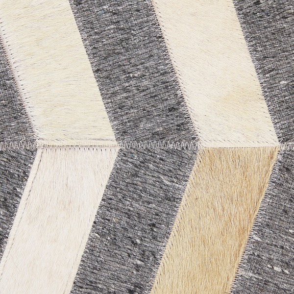 Nahaufnahme eines Patchwork-Teppichs aus echtem Kuhfell mit Chevron-Muster und sichtbaren Zickzack-Nähten.
