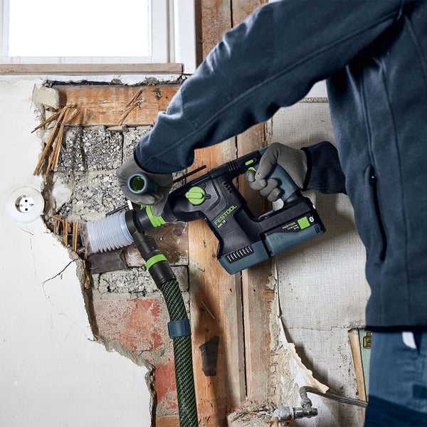 Ein Mann arbeitet mit einem Akku-Bohrhammer von Festool an einer Wand, an die ein Saugschlauch angeschlossen ist.