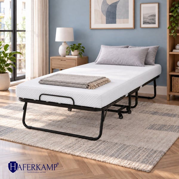 Haferkamp Klappbett mit Matratze in einem modern eingerichteten Schlafzimmer mit Holzregal und Teppich
