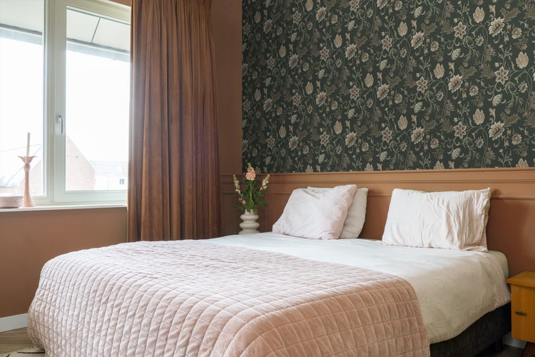 Schlafzimmer mit Bett, Vorhängen und floraler Tapete für eine gemütliche Atmosphäre