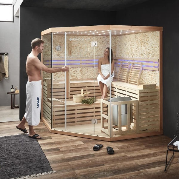 Moderne Ecksauna mit Glaselementen und Holzverkleidung in einem Innenraum mit zwei Personen, Saunazubehör und integrierter Beleuchtung.