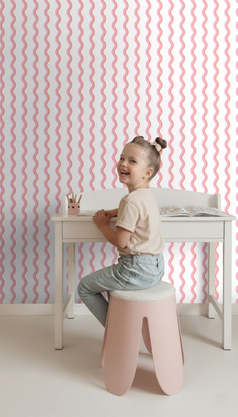 Mädchen sitzt an einem Schreibtisch vor einer Tapete mit Wellenmuster