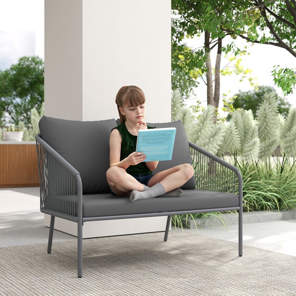 Kind sitzt lesend auf einem modernen 2-Sitzer Gartensofa mit Seilgeflecht-Rahmen und Polstern auf einer Terrasse mit Pflanzen.