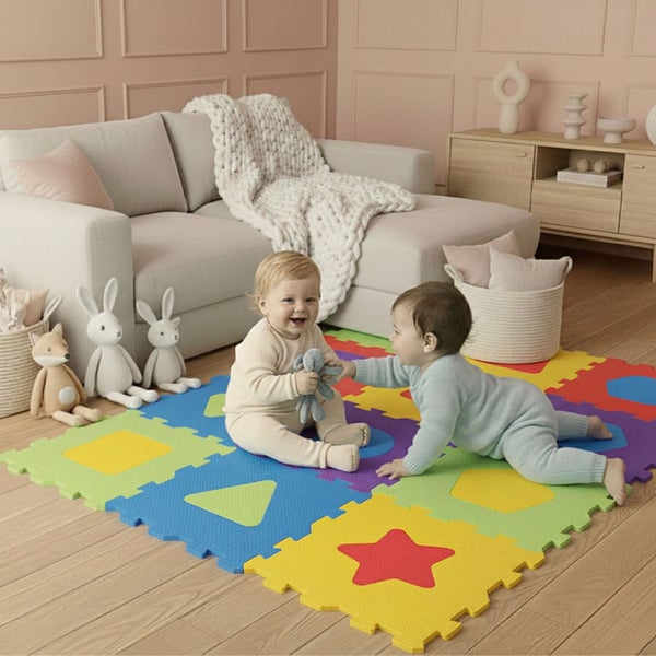 Zwei Babys spielen auf einer bunten Schaumstoff-Puzzlematte mit verschiedenen Formen auf hellem Holzboden in einem hellen, aufgeräumten Wohnzimmer.