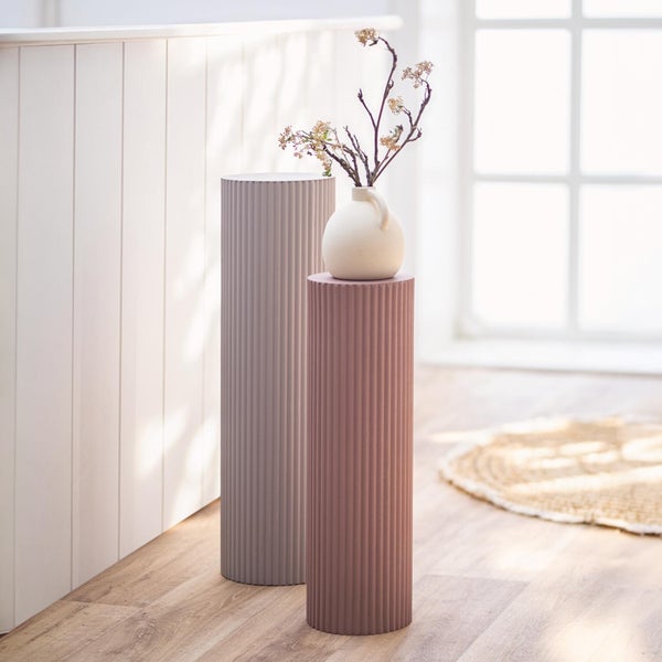 Zwei dekorative zylindrische Sockel mit gerillter Oberfläche in einem hellen Raum zur Präsentation von Wohnaccessoires wie einer Vase.