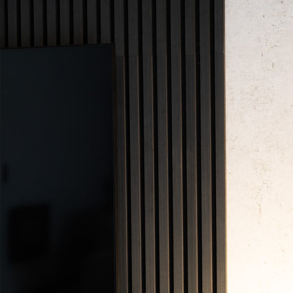 Wandpaneele aus dunklen Holzlamellen neben einem schwarzen Bildschirm an einer hellen Wand.