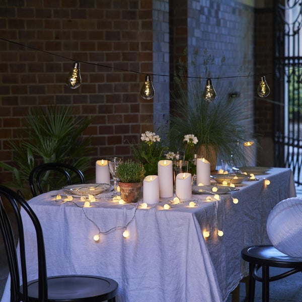 Gedeckter Tisch mit Tischdecke, Geschirr, Pflanzen, LED Kerzen und Lichterketten im Außenbereich.