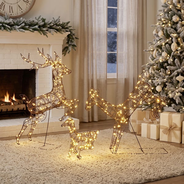 Beleuchtete Rentierfamilie aus Drahtgeflecht als weihnachtliche Dekoration in einem gemütlich eingerichteten Wohnzimmer mit Kamin und Weihnachtsbaum.