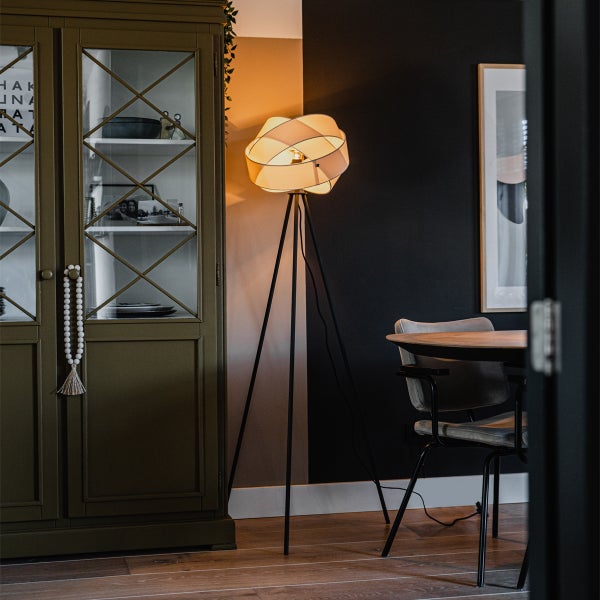 Dreibein-Stehleuchte mit gewebtem Schirm in einem modernen Wohnzimmer neben einem grünen Vitrinenschrank und einem Esstisch aus Holz.