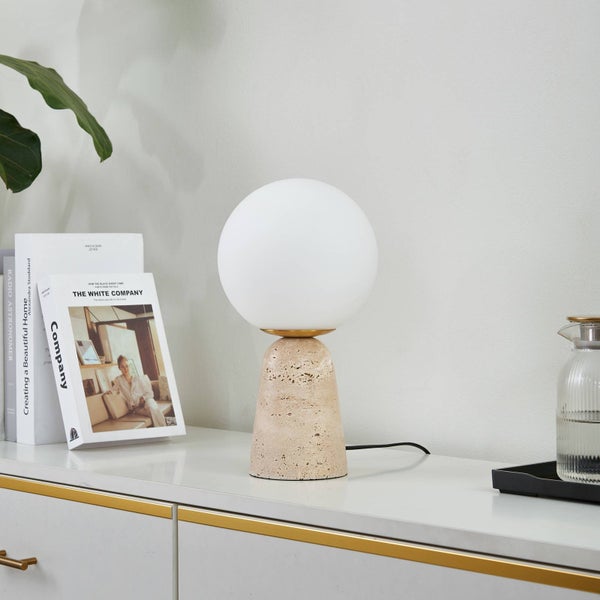 Moderne Tischleuchte mit weißer Glaskugel und kegelförmigem Sockel aus Travertin-Naturstein auf einem Sideboard.