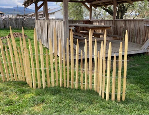 Holzzaun mit spitz zulaufenden Pfählen auf einer Rasenfläche