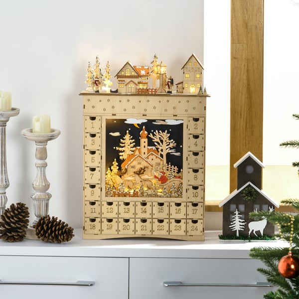 Beleuchteter Adventskalender aus Holz mit 24 Schubladen und winterlicher Szene auf einem weißen Sideboard neben Kerzenständern und Tannenzapfen.