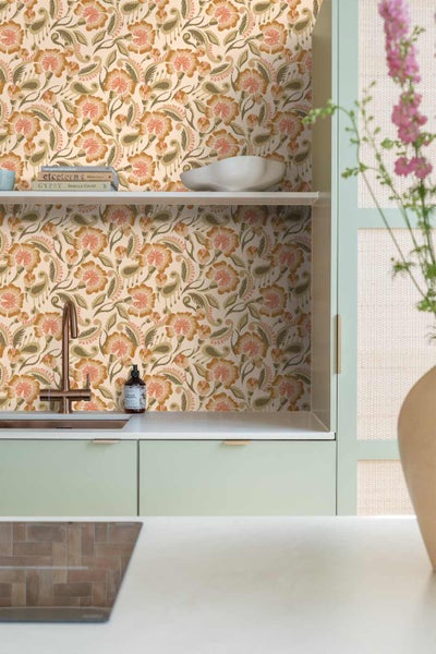 Helle Küche mit floraler Tapete, hellgrünen Schränken, weißer Arbeitsplatte und kupferfarbener Armatur.
