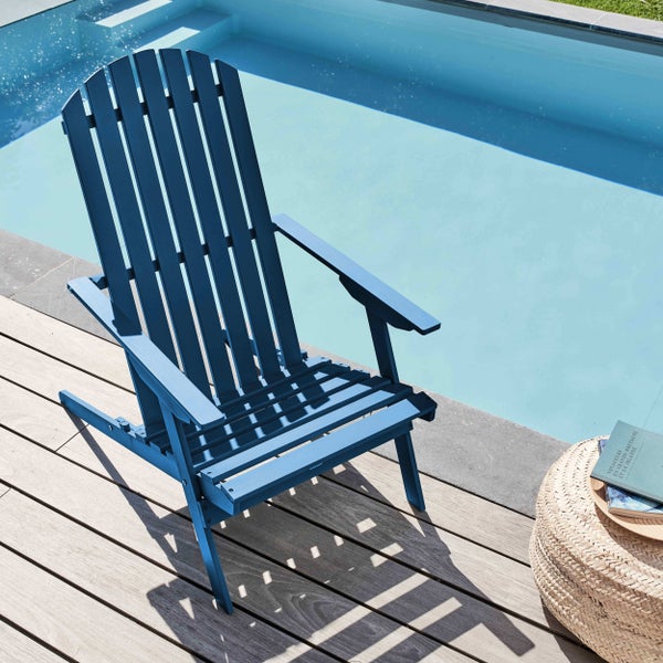 Blauer Adirondack Gartenstuhl aus Holz auf einer Holzterrasse an einem Swimmingpool mit einem geflochtenen Hocker.