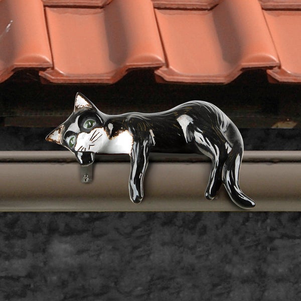 Dachfigur Katze aus Keramik in Schwarz und Weiß, liegend auf einer Dachrinne.