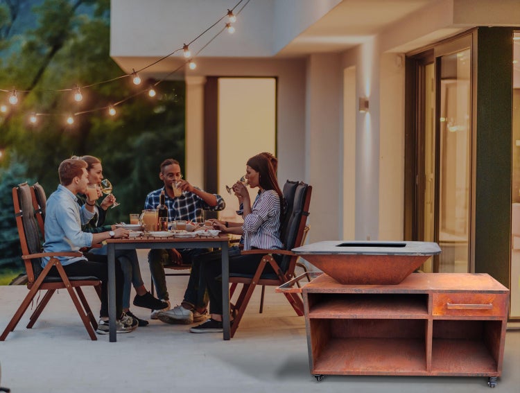 Szene im Freien mit einer Gruppe von Menschen, die an einem Tisch sitzen und essen. Im Vordergrund befindet sich ein Grillwagen mit Grill.