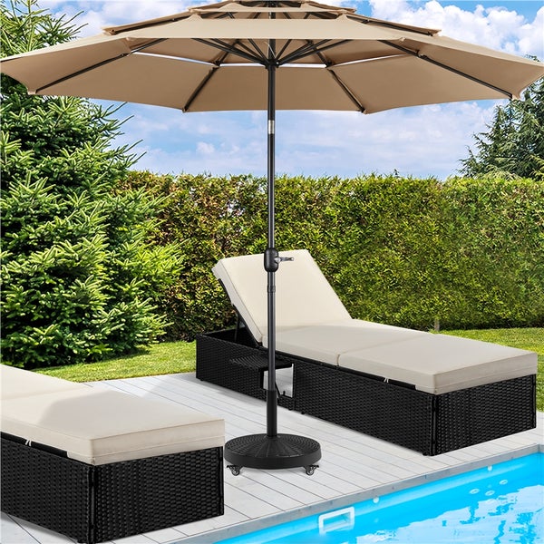 Großer beige Sonnenschirm mit schwarzem Mast auf einer Terrasse neben einem Pool mit Gartenliegen aus schwarzem Geflecht und grüner Hecke.