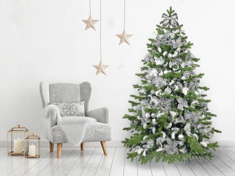 Geschmückter Weihnachtsbaum mit silberner Dekoration neben einem Sessel und hängenden Sternen in einem weihnachtlich eingerichteten Raum.