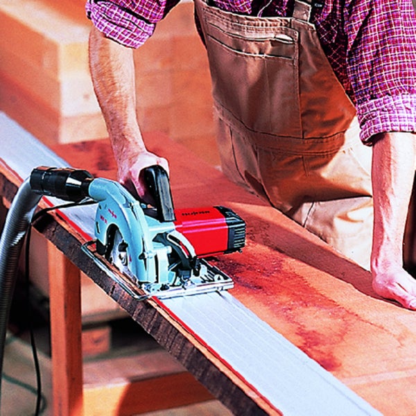 Handwerker beim Zuschneiden eines Holzbretts mit einer Tauchsäge inklusive Führungsschiene und Absaugschlauch.