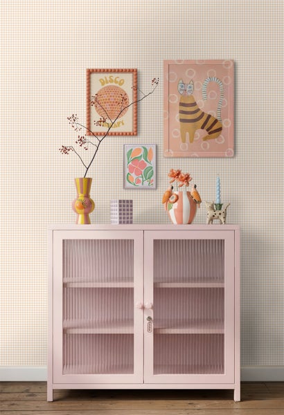 Karierte Tapete hinter einer rosa Metallvitrine mit geriffeltem Glas, dekoriert mit bunten Vasen und Wandbildern in einem hellen Raum.
