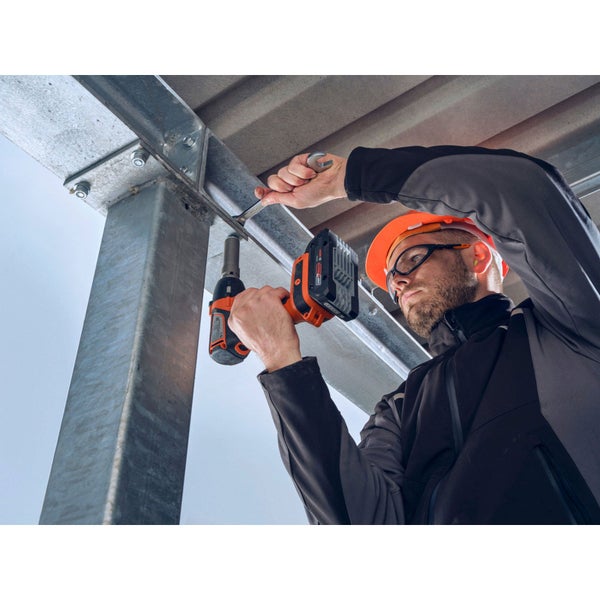 Ein Mann mit Schutzhelm und Schutzbrille arbeitet mit einem Akku-Schlagschrauber an einer Metallkonstruktion.