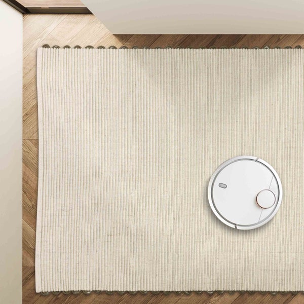 Draufsicht auf einen hellen, gerippten Teppich auf Parkettboden mit einem weißen Saugroboter.