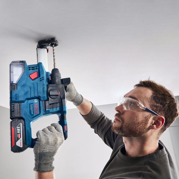 Ein Mann bohrt mit einem Bohrhammer ein Loch in die Decke. Er trägt eine Schutzbrille und Handschuhe.
