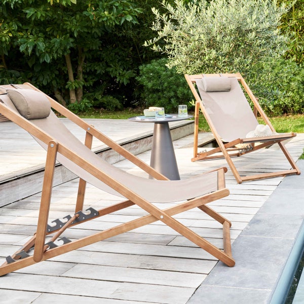 Zwei klappbare Gartenliegen aus Holz mit beigem Textilbezug und Kopfpolster auf einer Holzterrasse neben einem Pool.