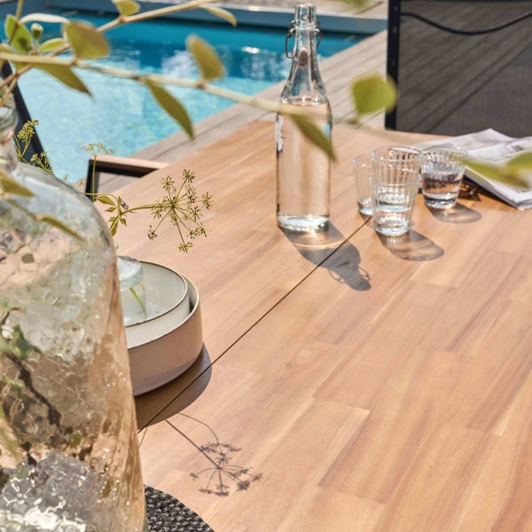 Gedeckter Gartentisch aus Holz mit Wasserflasche und Gläsern auf einer Terrasse am Pool.