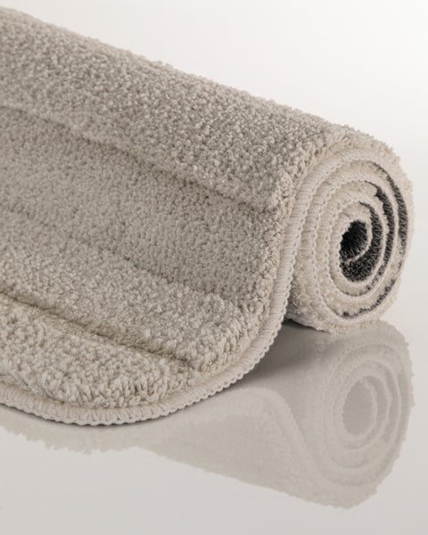 Aufgerollter, weicher Badteppich mit strukturierter Oberfläche und hochwertiger Kettelung.
