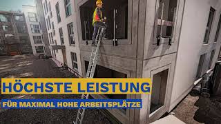 Eine Person mit Helm und Sicherheitsweste steht auf einer Leiter an einem mehrstöckigen Gebäude.