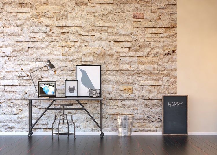 Helles Arbeitszimmer mit Schreibtisch, Stuhl, Laptop, Stehlampe, Dekoration und Tafel vor einer Steinwand