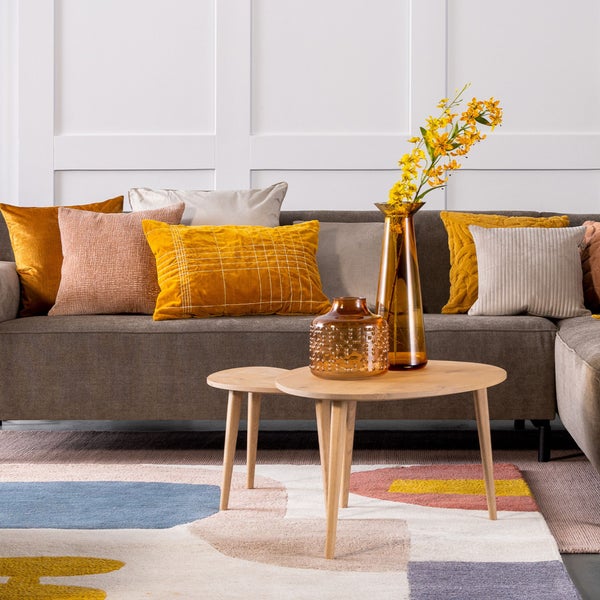 Wohnzimmer-Szene mit Sofa, Kissen, Couchtisch, Vasen, Blumen und Teppich für eine gemütliche Atmosphäre.