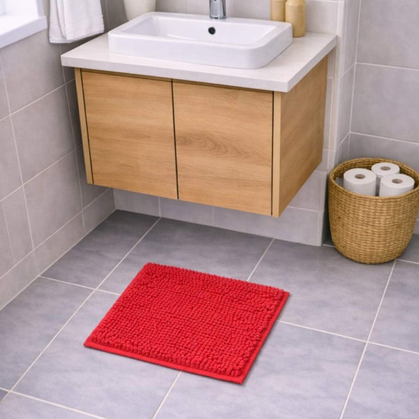 Roter Badeteppich aus Chenille vor einem hölzernen Waschbeckenunterschrank in einem hellen, modern gefliesten Badezimmer.