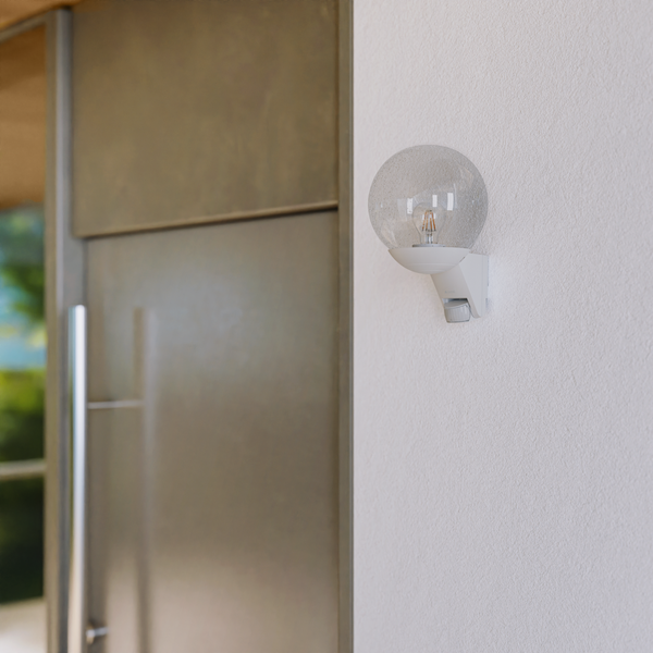 Moderne Außenwandleuchte in Kugelform mit Bewegungsmelder und Glasschirm montiert an einer Hauswand neben einer Tür.