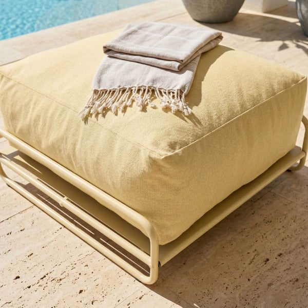 Outdoor-Pouf mit Metallgestell und großem Polsterkissen auf einer Terrasse am Pool.
