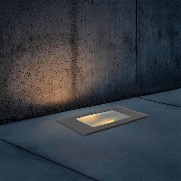 Rechteckiger Bodeneinbaustrahler für den Außenbereich, der eine Betonwand mit warmem Licht von unten anstrahlt.