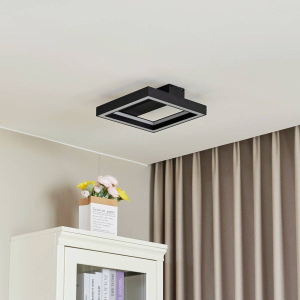 Schwarze quadratische Deckenleuchte mit zwei Lichtrahmen an weißer Zimmerdecke über einem weißen Schrank mit Blumen.