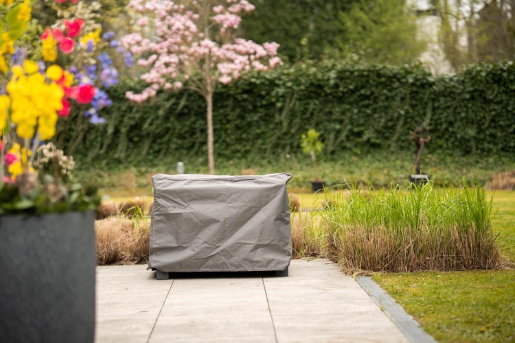 Abgedeckte Gartenmöbel auf einer Terrasse mit Pflanzen im Hintergrund
